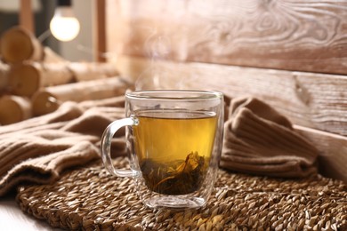 Photo of Wicker mat with freshly brewed tea near wooden wall in room. Cozy home atmosphere