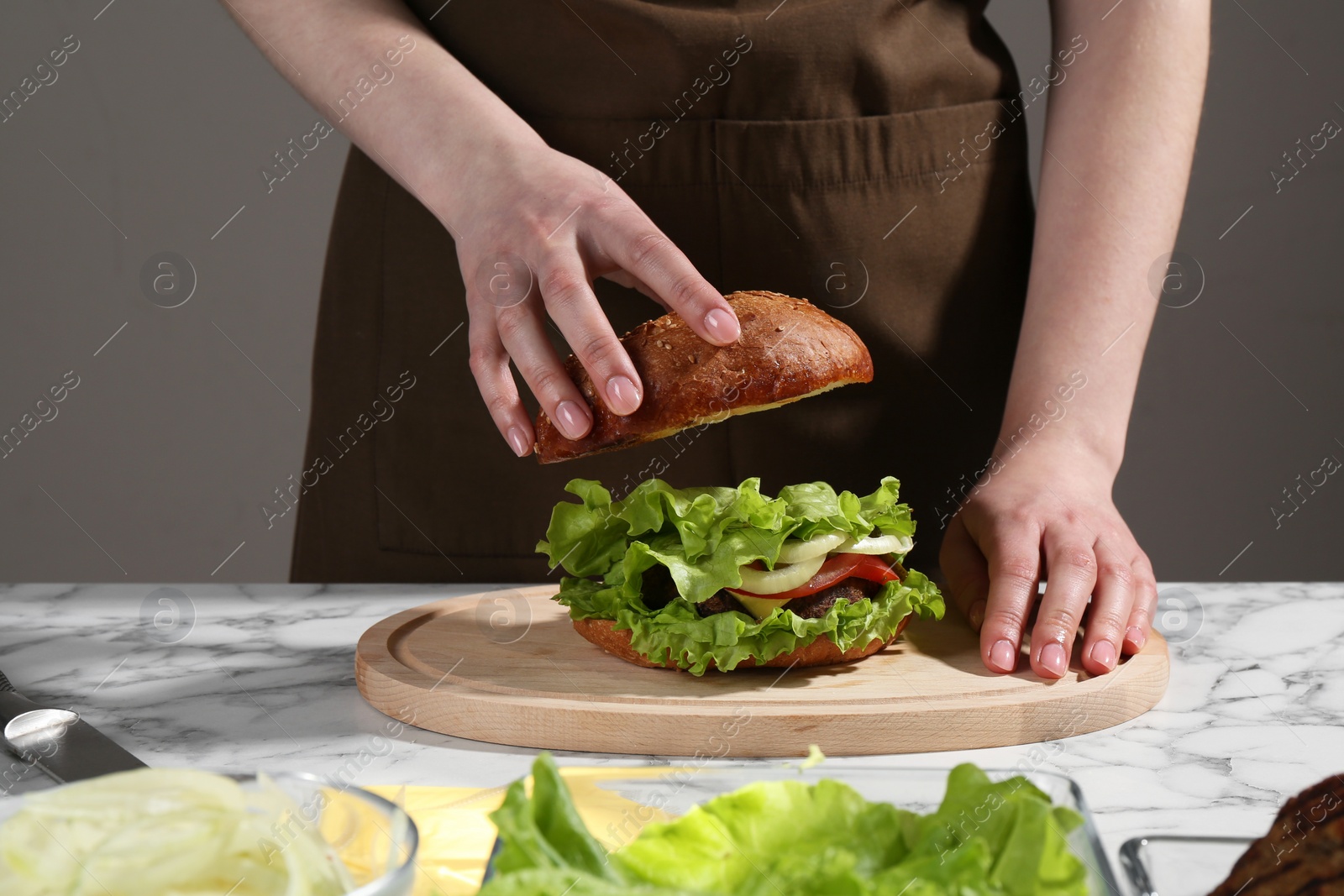 Photo of Woman making delicious vegetarian burger at white marble table, closeup