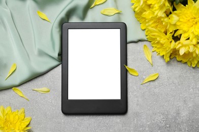 Photo of E-book reader with fabric and flowers on grey stone table, flat lay. Space for text