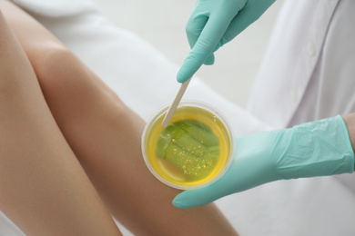 Photo of Woman getting wax epilation of legs in salon, closeup