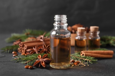 Bottle of essential oil, anise, cinnamon and fir tree branches on black table