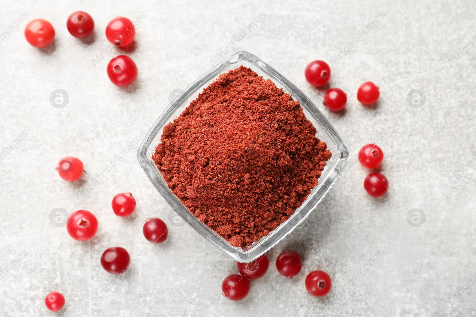 Photo of Cranberry powder in bowl and fresh berries on light grey table, top view