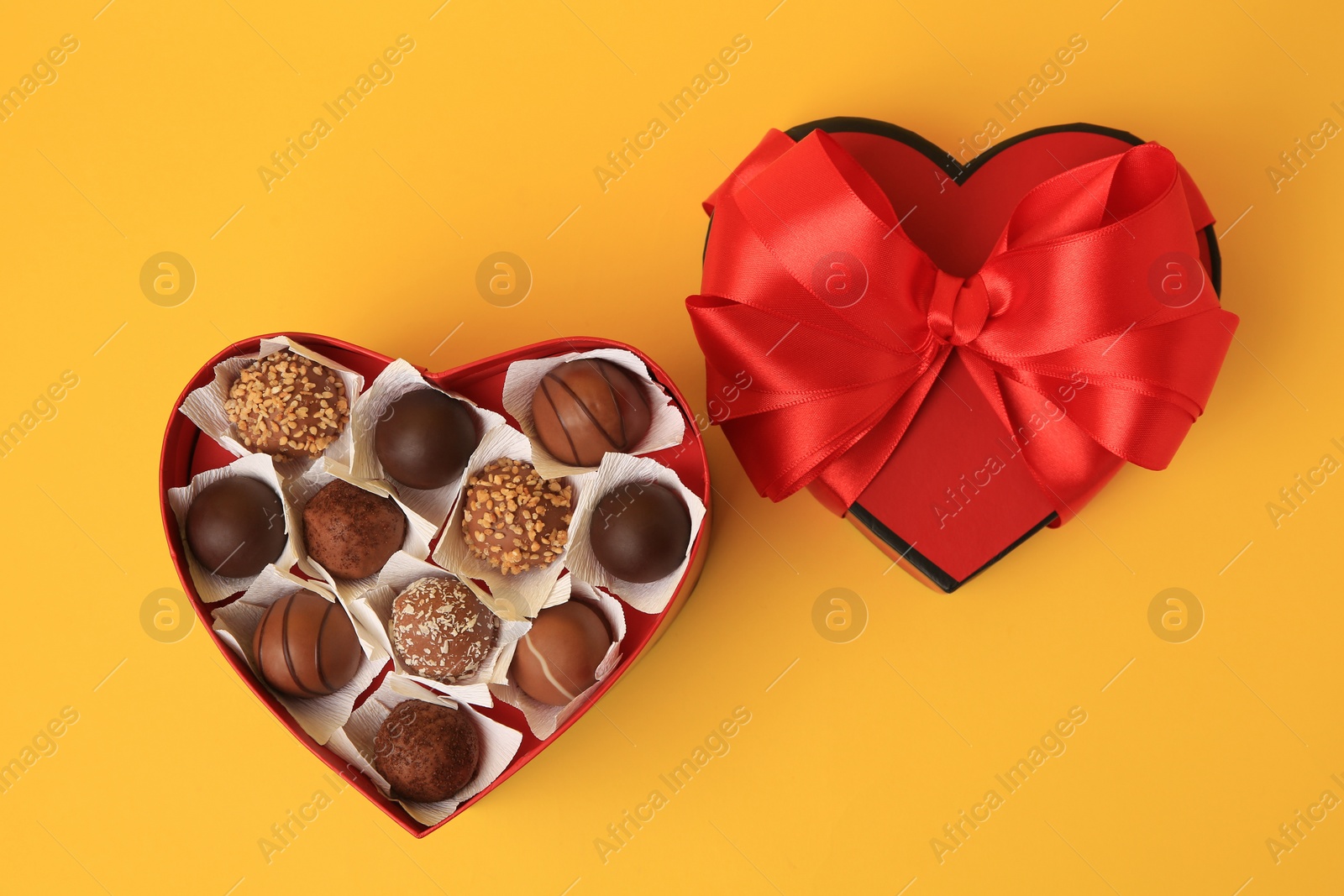 Photo of Heart shaped box with delicious chocolate candies on yellow background, flat lay