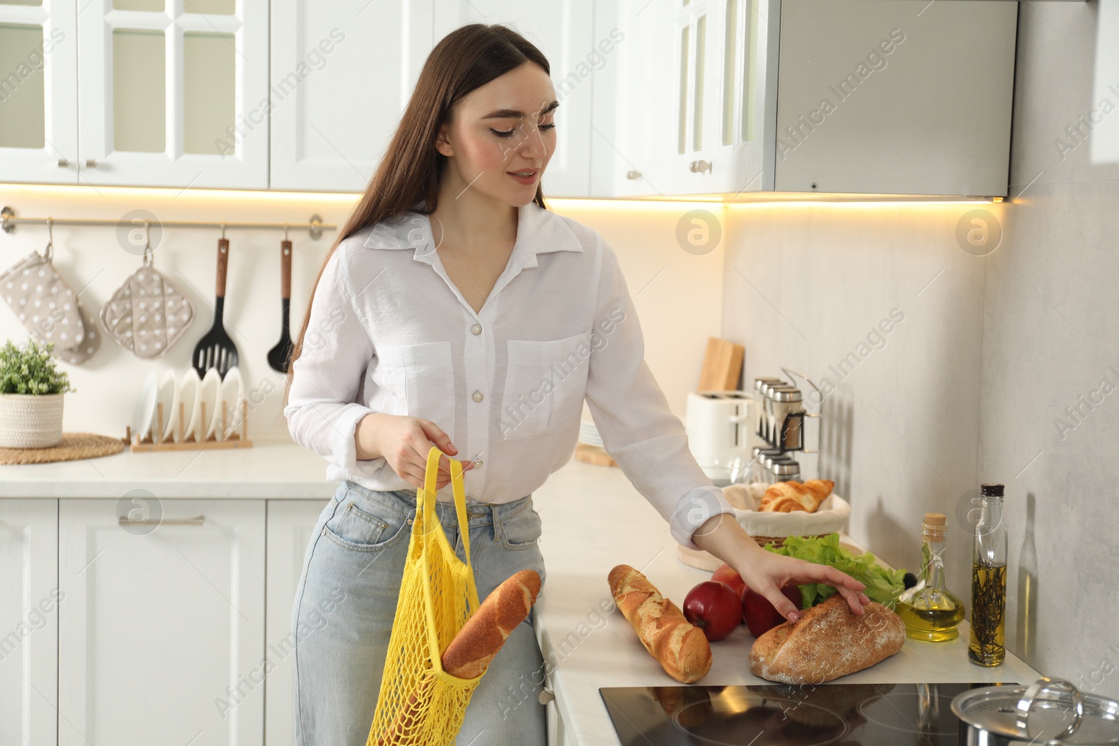 Photo of Woman holding string bag with baguette in kitchen