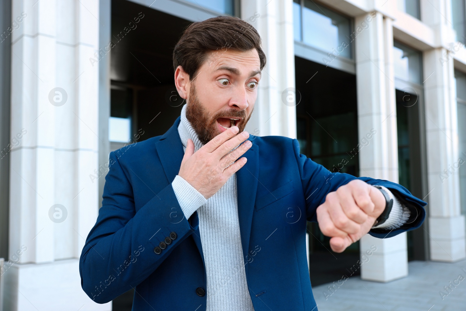 Photo of Emotional businessman looking at watch near building. Being late concept