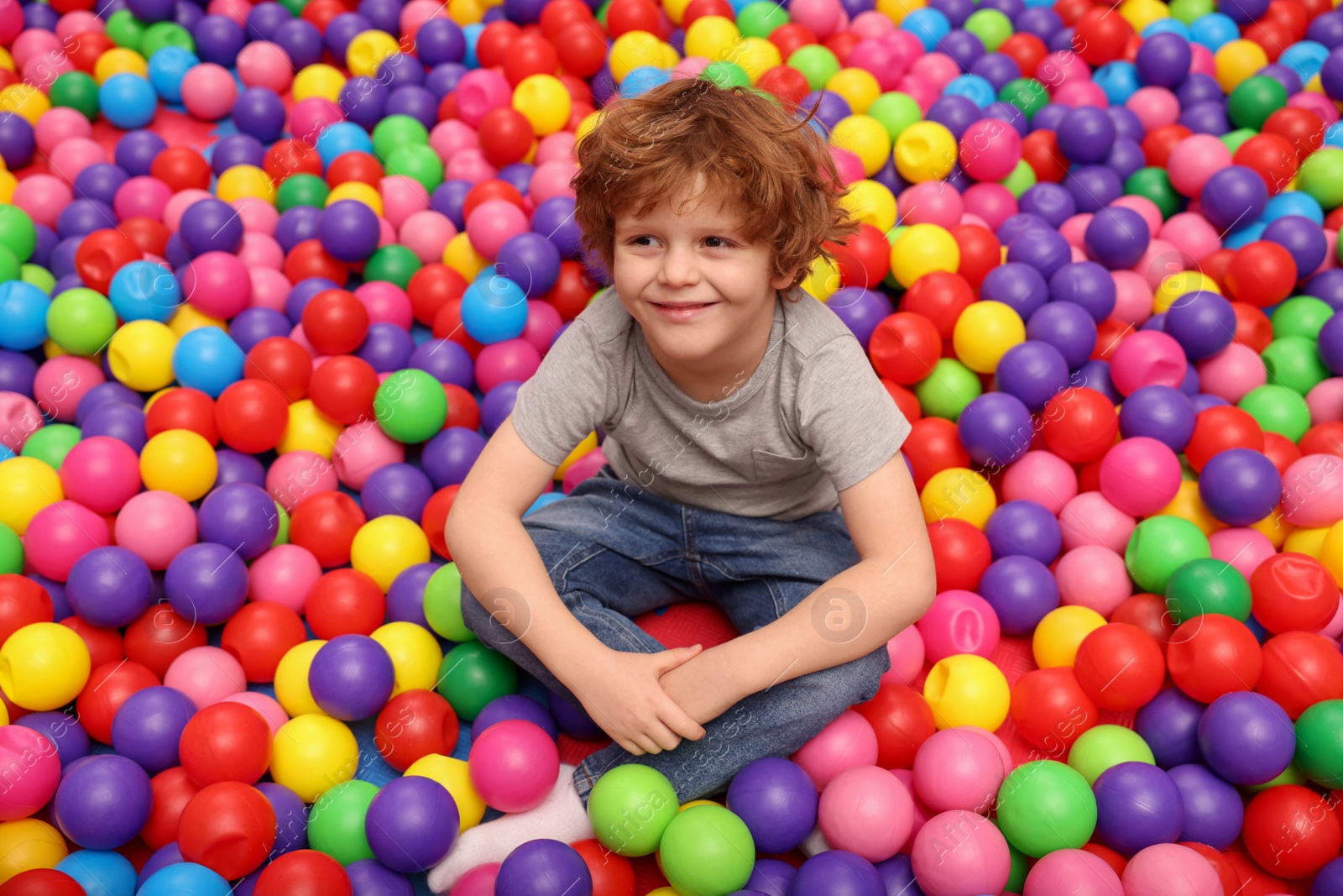 Photo of Happy little boy sitting on colorful balls in ball pit