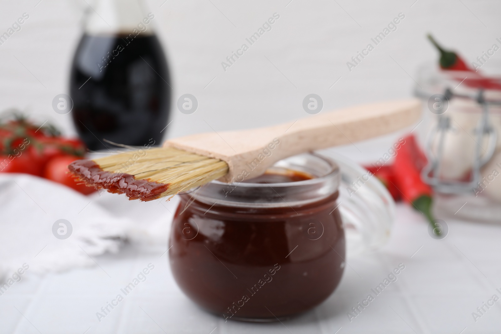 Photo of Marinade in jar and basting brush on white table, closeup
