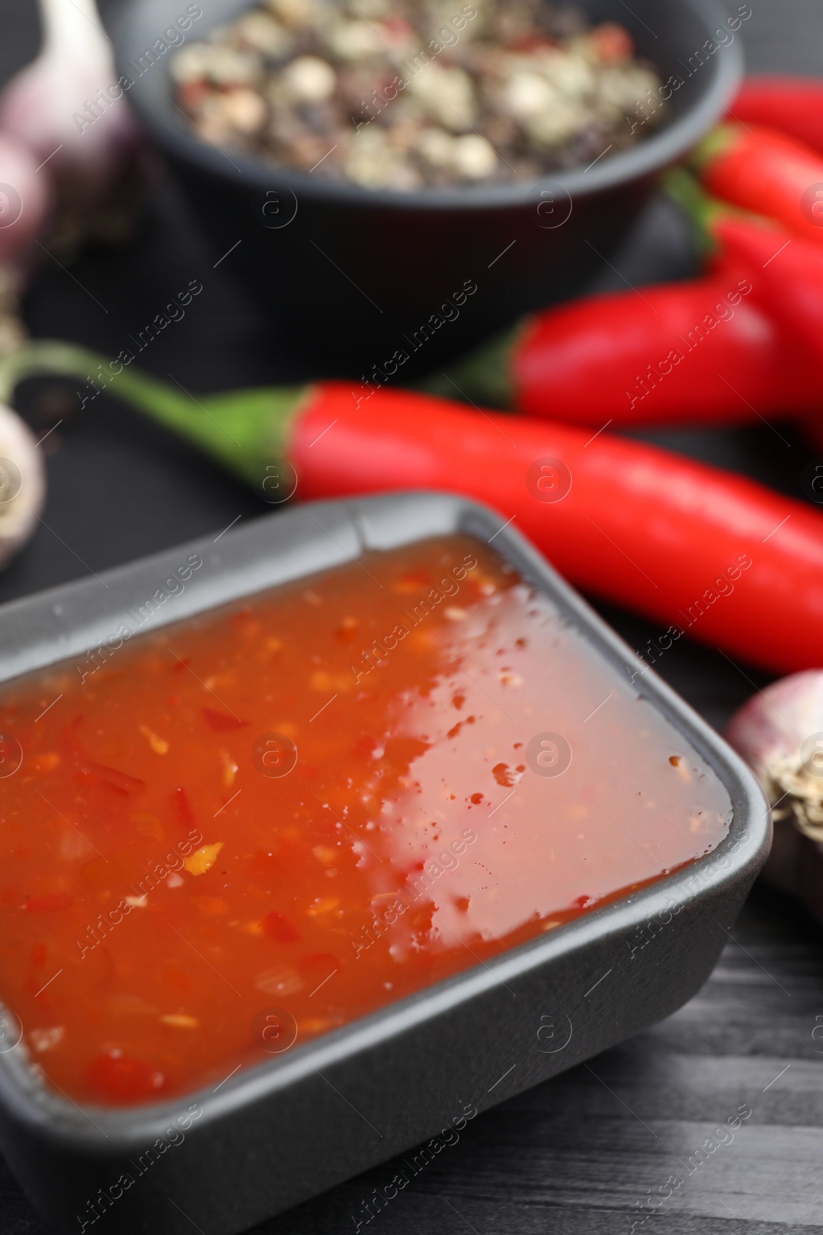 Photo of Spicy chili sauce in bowl on black wooden table, closeup