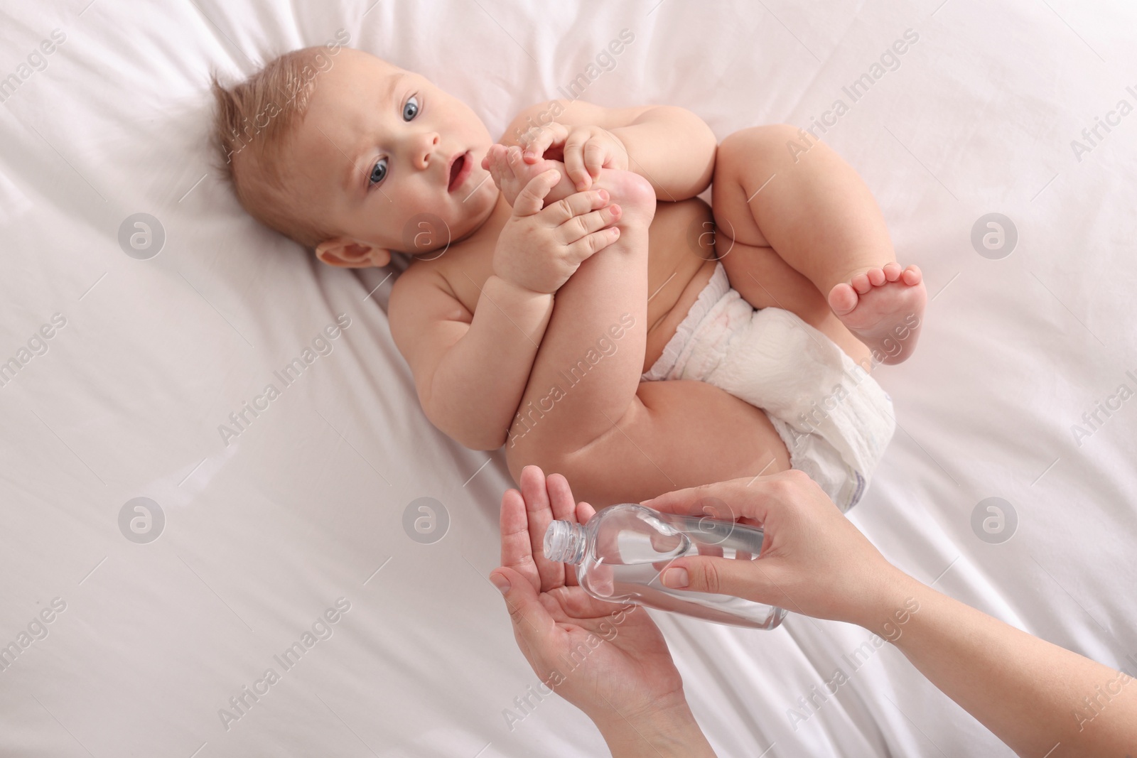 Photo of Mother with bottle of massage oil near baby on bed, closeup