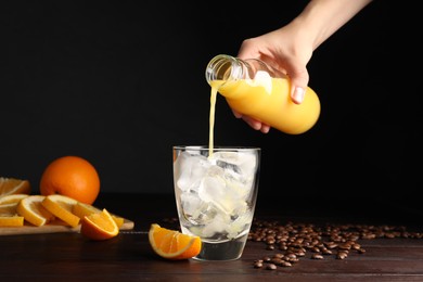 Photo of Woman pouring orange juice into glass with ice cubes at wooden table, closeup