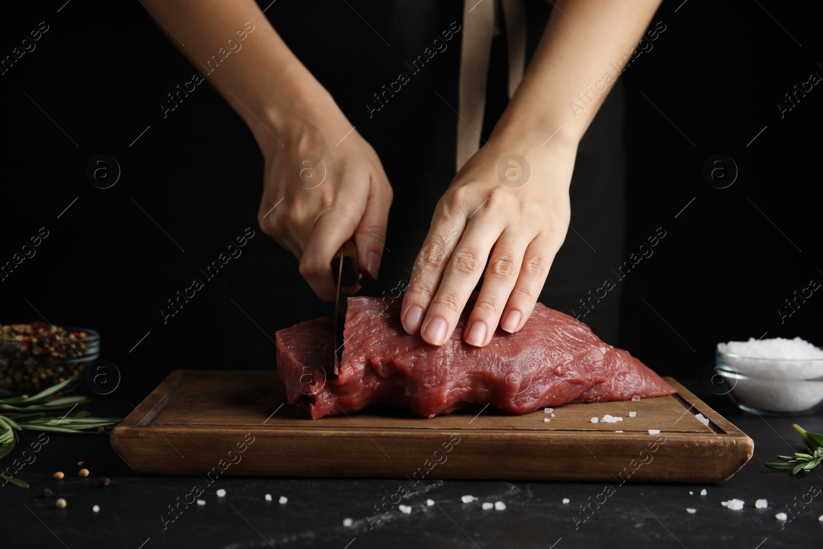 Photo of Woman cutting fresh raw meat at black table, closeup