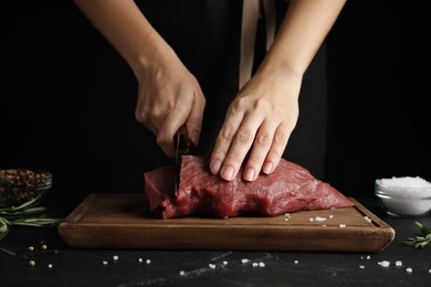 Woman cutting fresh raw meat at black table, closeup