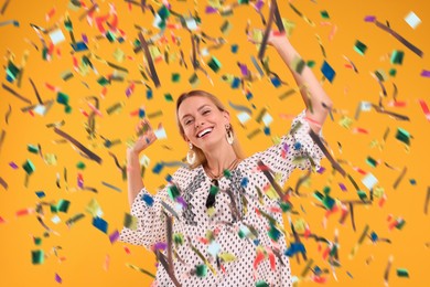 Happy woman dancing under falling confetti on orange background