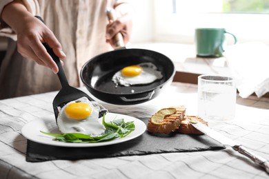 Photo of Woman putting tasty fried eggs onto plate at table indoors, closeup