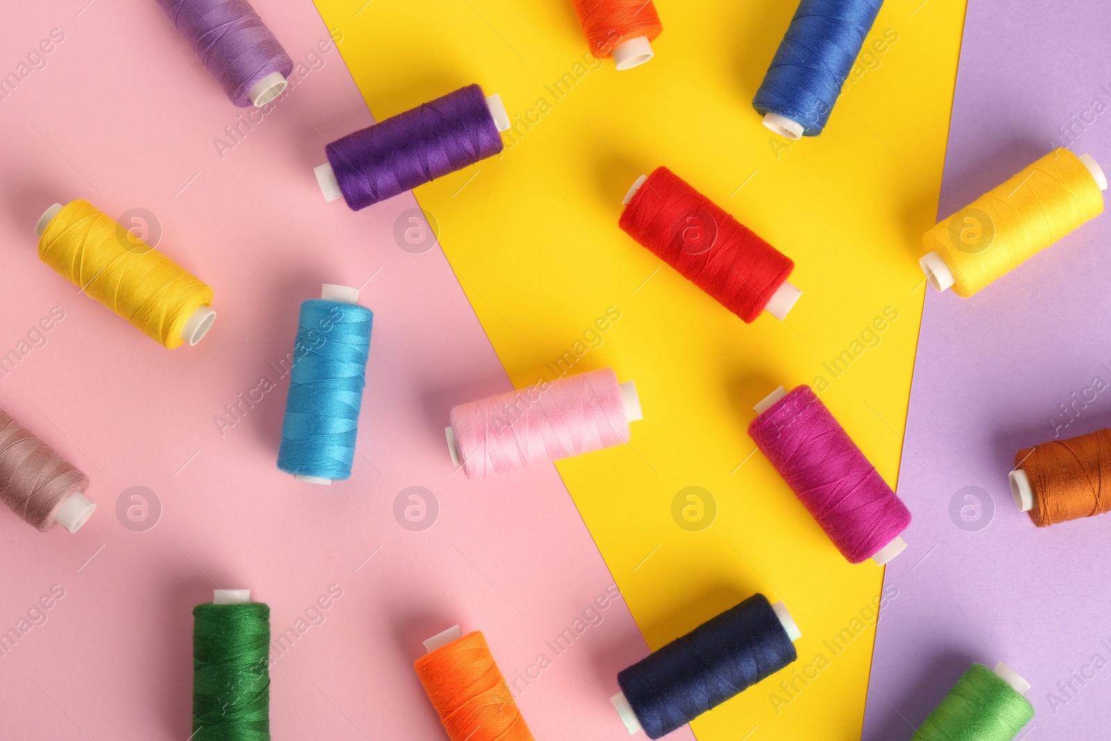 Photo of Different sewing threads on color background, flat lay