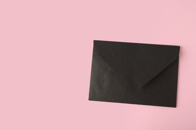 Photo of Black paper envelope on pink background, top view. Space for text