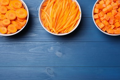 Photo of Bowls with cut fresh juicy carrots on blue wooden table, flat lay. Space for text
