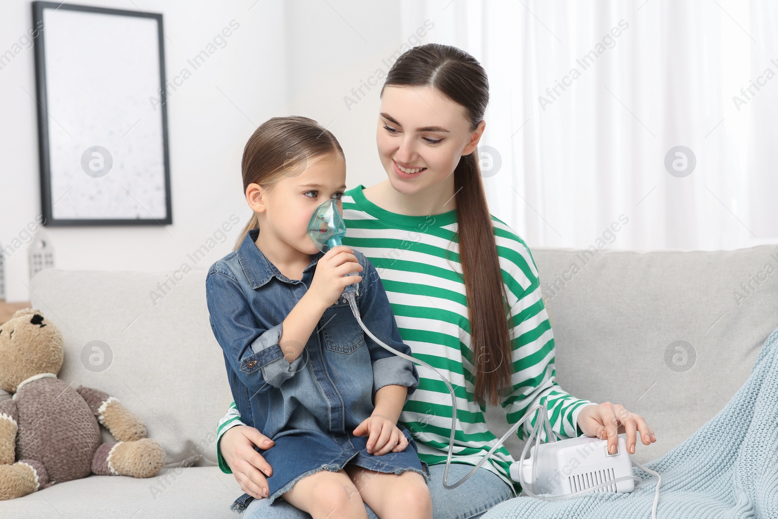 Photo of Mother helping her sick daughter with nebulizer inhalation at home