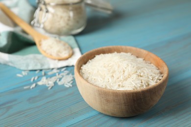 Photo of Raw basmati rice in bowl on light blue wooden table, closeup