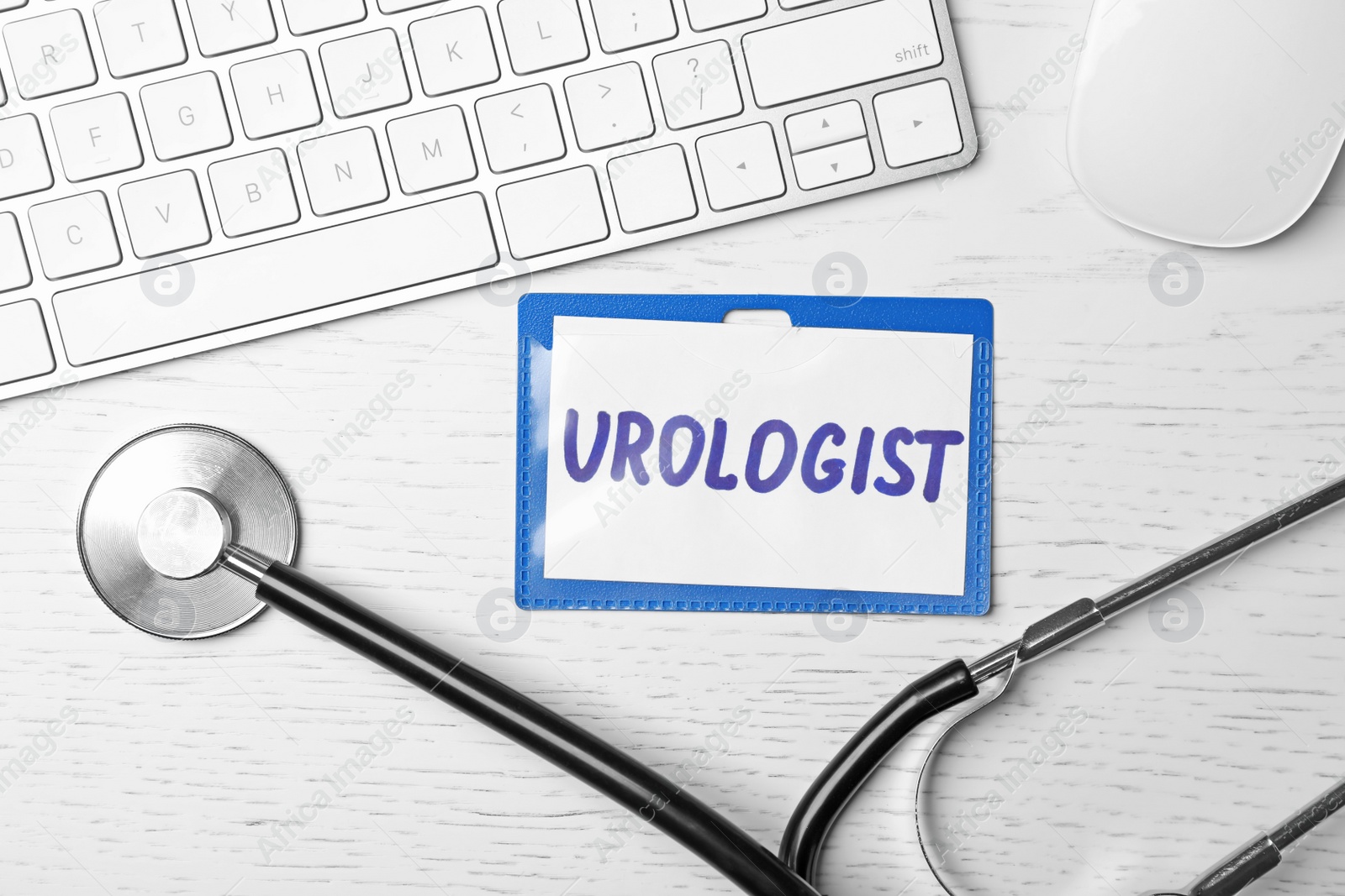 Photo of Badge with inscription UROLOGIST, keyboard and stethoscope on table, top view