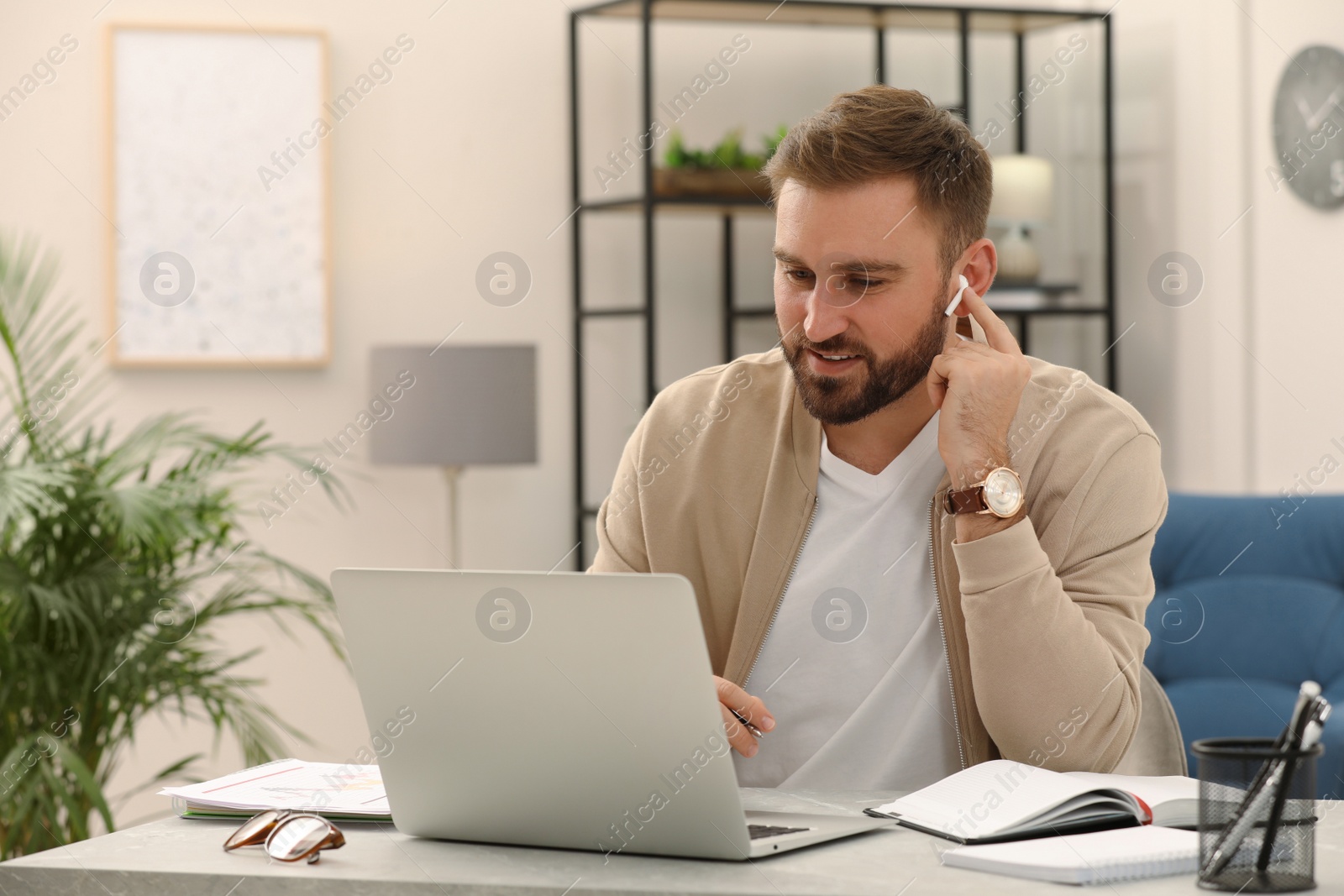 Photo of Young man with earphones having video call on laptop indoors. Working from home