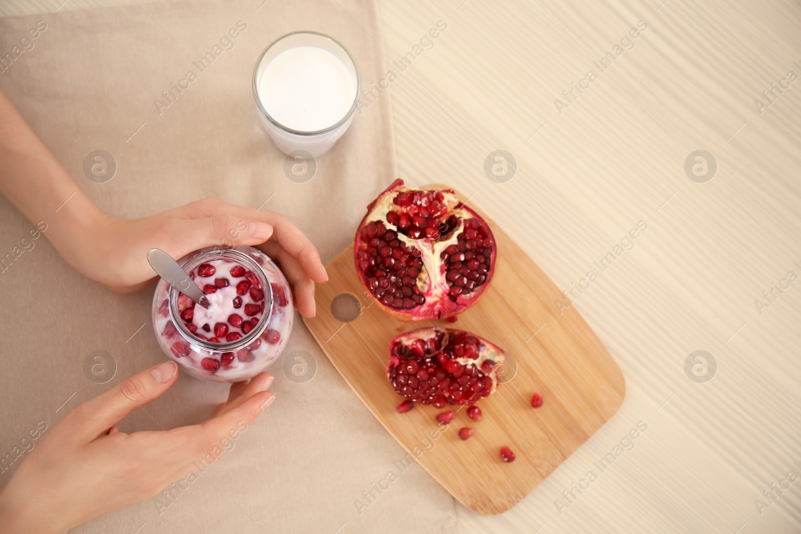 Photo of Young woman eating tasty yogurt with pomegranate seeds at table