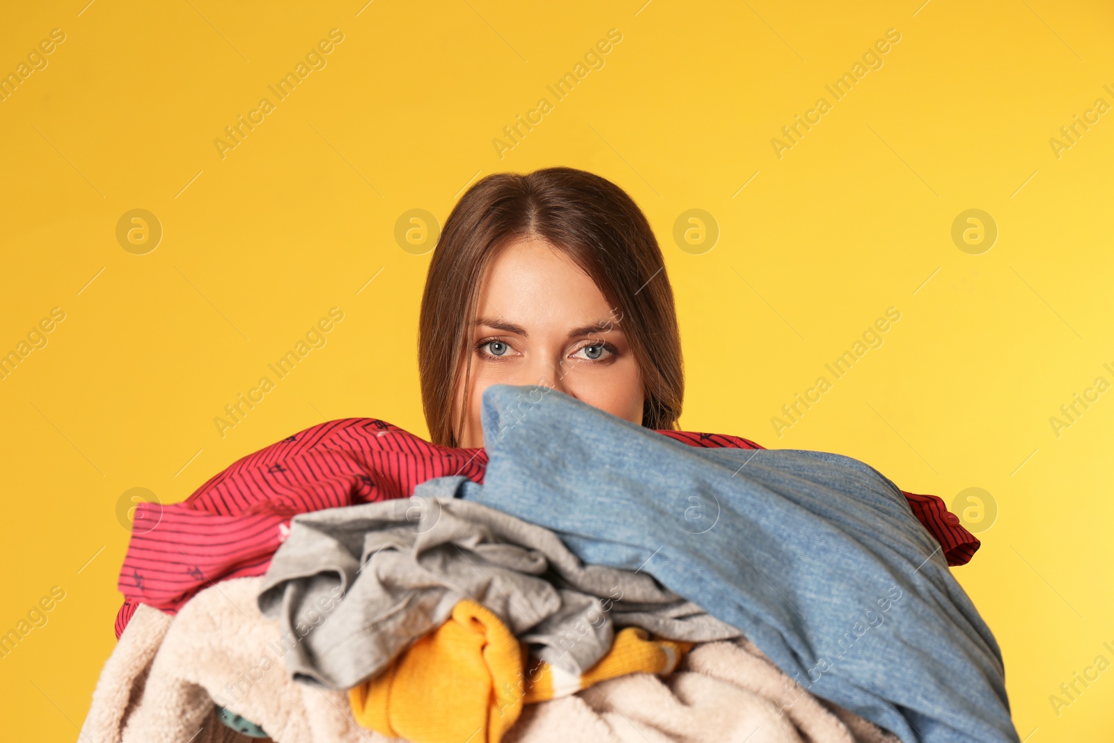 Photo of Young woman holding pile of dirty laundry on color background