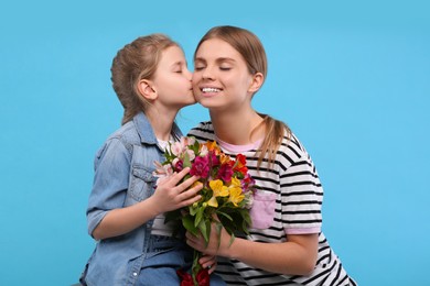 Photo of Little daughter congratulating her mom with flowers on light blue background. Happy Mother's Day