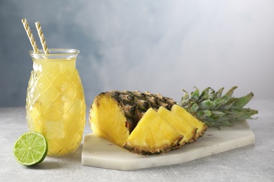 Photo of Delicious pineapple juice and fresh fruits on light grey table
