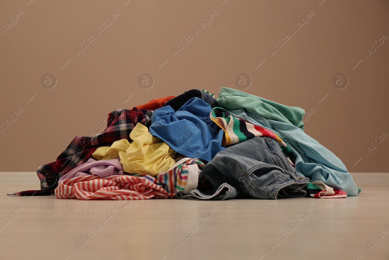 Photo of Pile of dirty clothes on floor near light brown wall indoors