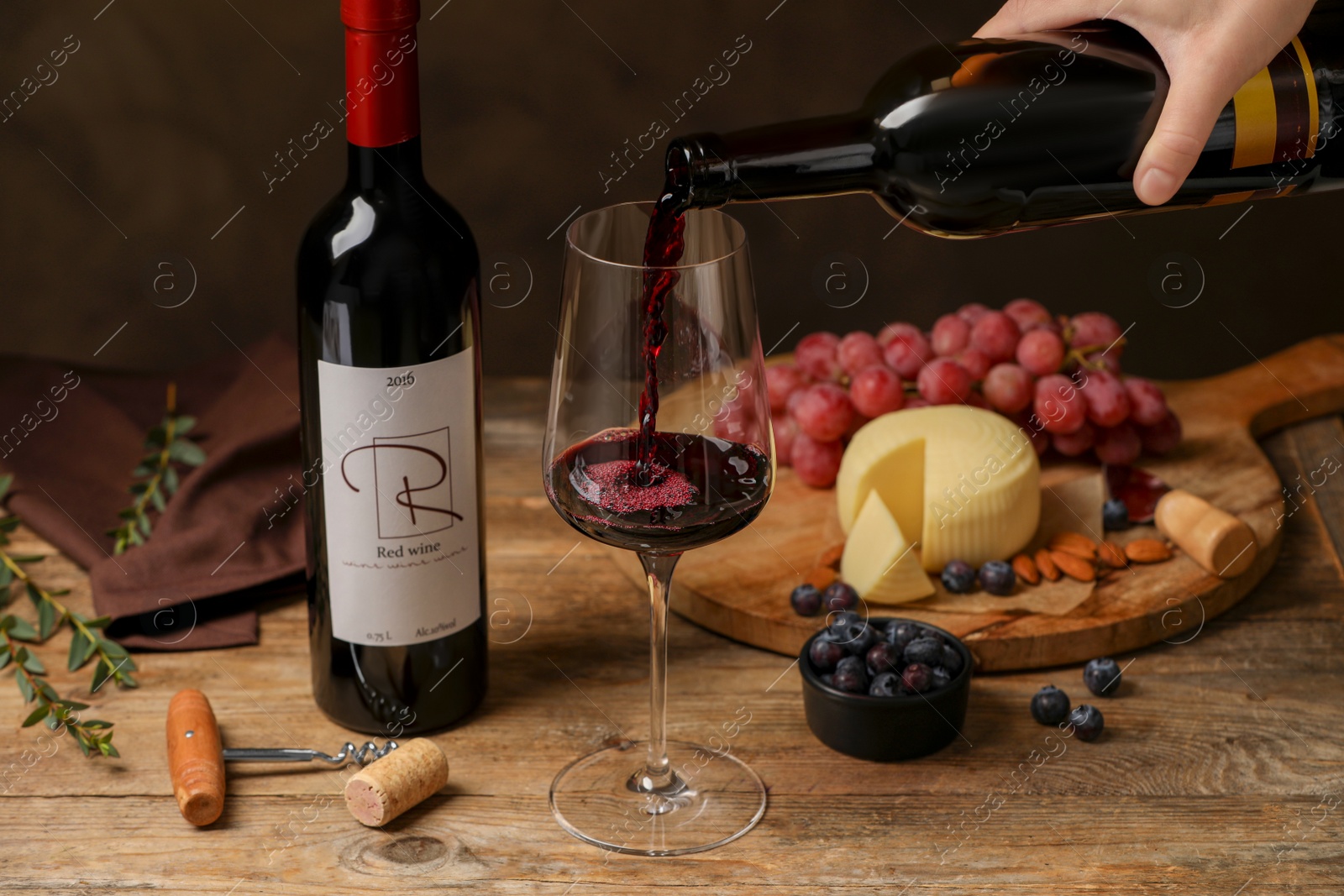 Photo of Woman pouring red wine into glass and appetizers on wooden table, closeup