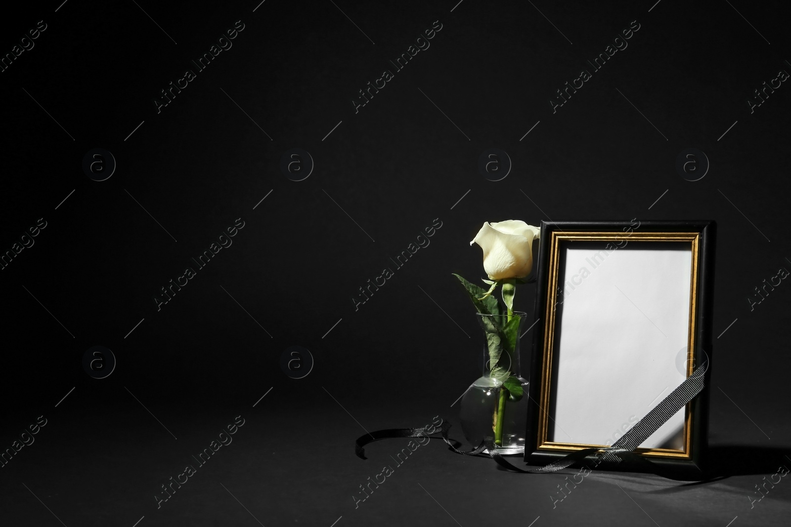 Photo of Funeral photo frame with ribbon and white rose on black background. Space for design