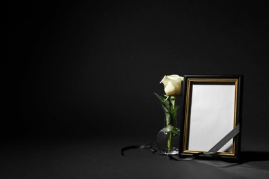Photo of Funeral photo frame with ribbon and white rose on black background. Space for design