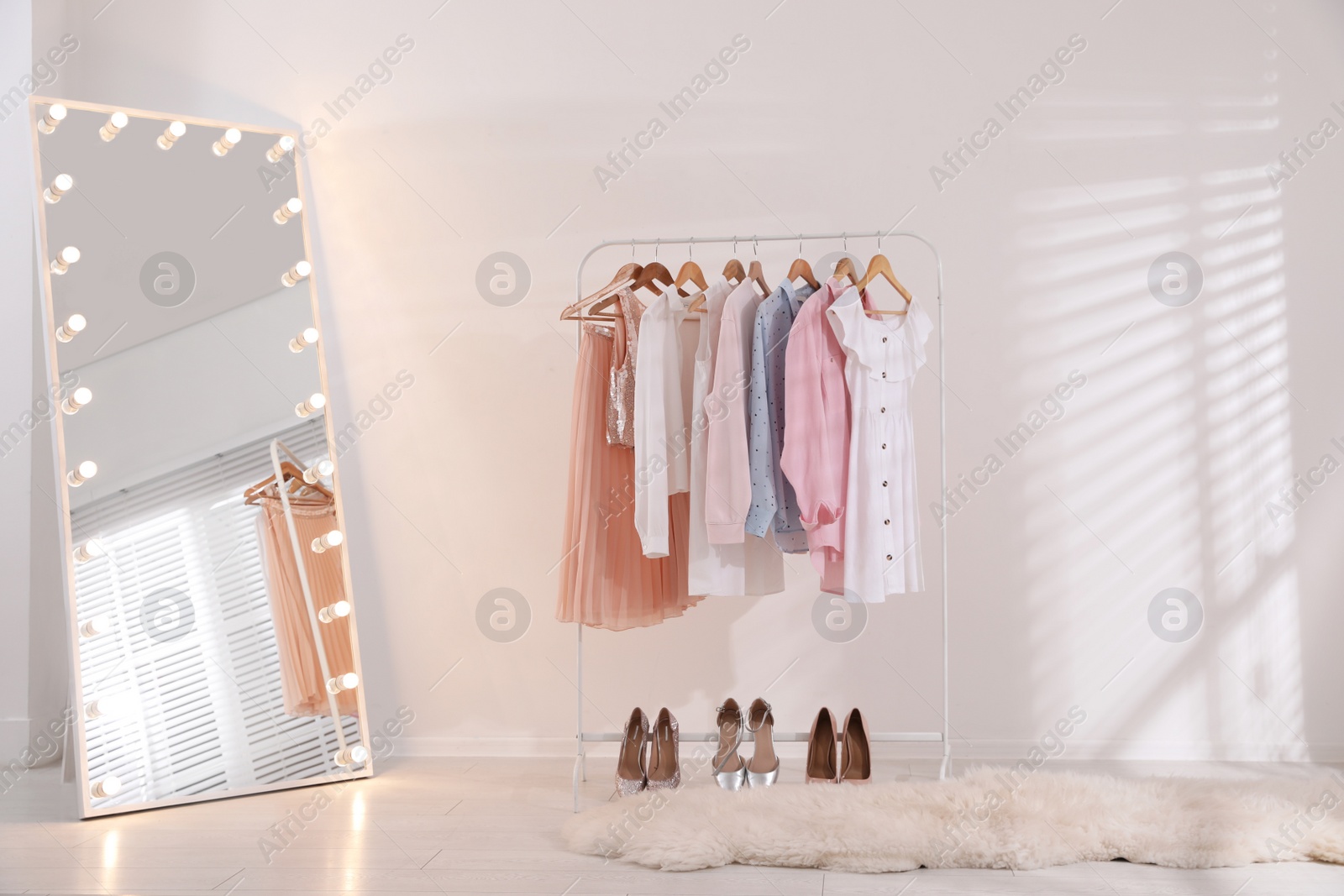 Photo of Rack with stylish women's clothes and mirror indoors. Interior design