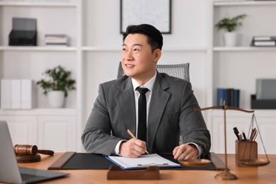 Photo of Happy notary writing notes at wooden table in office