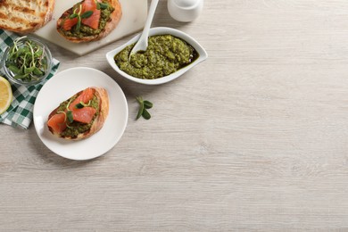 Photo of Delicious bruschettas with salmon and pesto sauce on wooden table, flat lay. Space for text