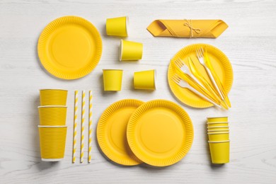 Yellow disposable tableware on white wooden background, flat lay