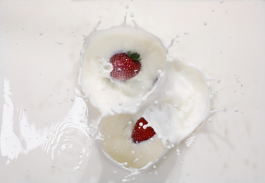Photo of Strawberries falling in milk with splashes, top view