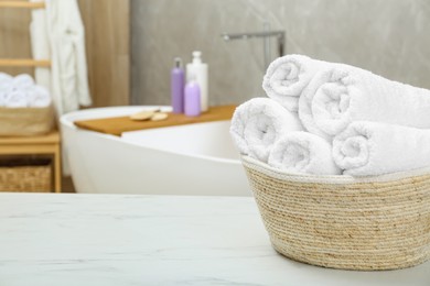 Photo of Wicker basket with rolled bath towels on white table in bathroom, space for text