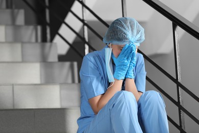 Photo of Exhausted doctor sitting on stairs in hospital, space for text