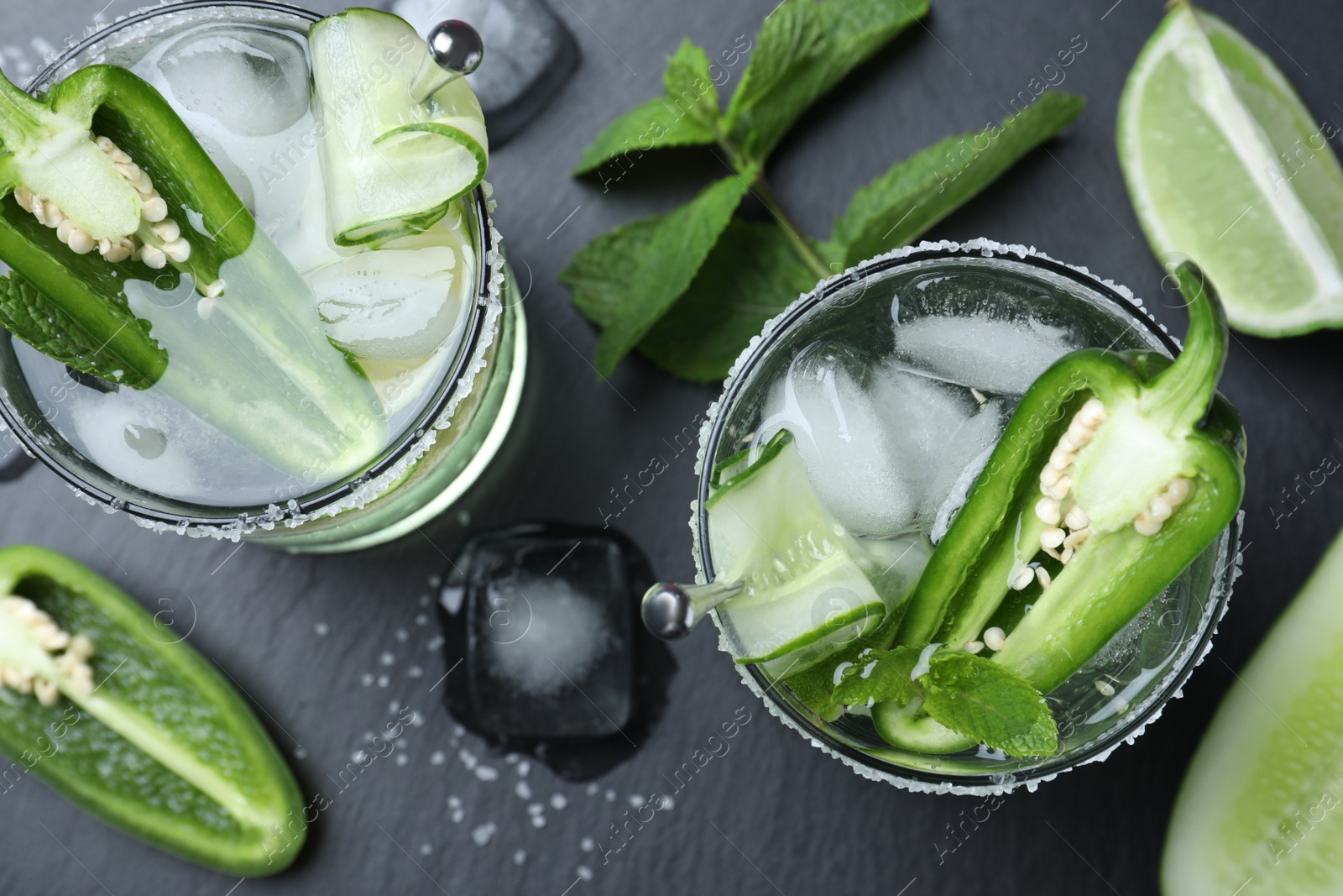 Photo of Spicy cocktail with jalapeno, cucumber and lime on black table, flat lay