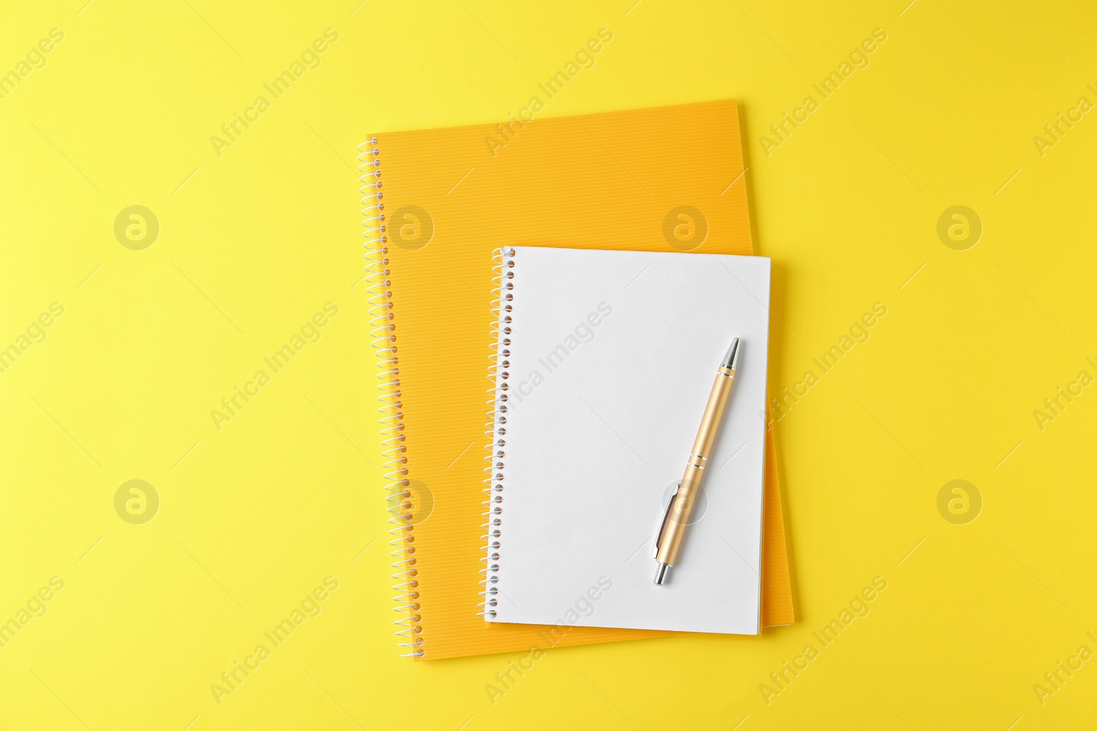 Photo of Notebooks and pen on yellow background, top view