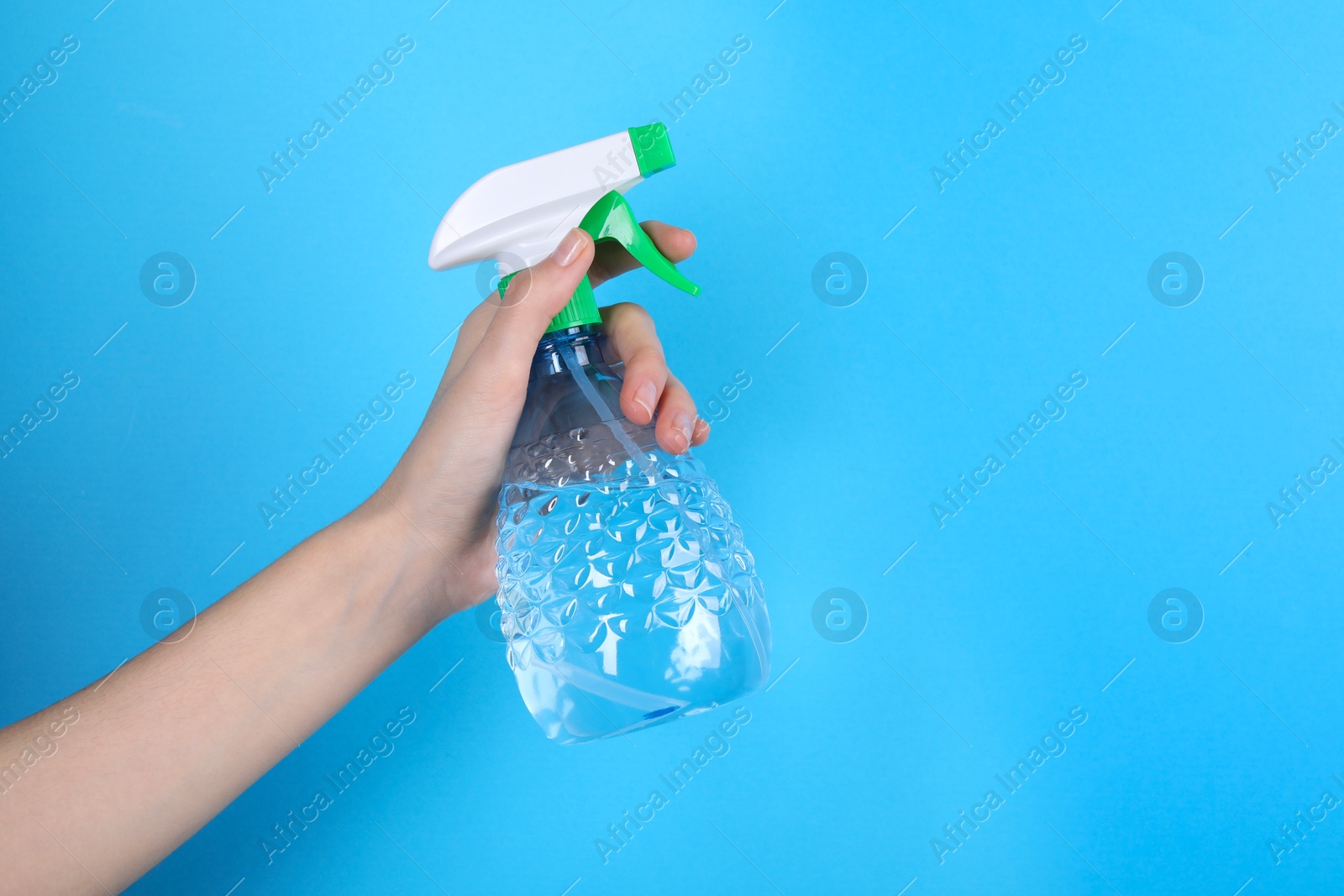 Photo of Woman holding plastic spray bottle on light blue background, closeup. Space for text