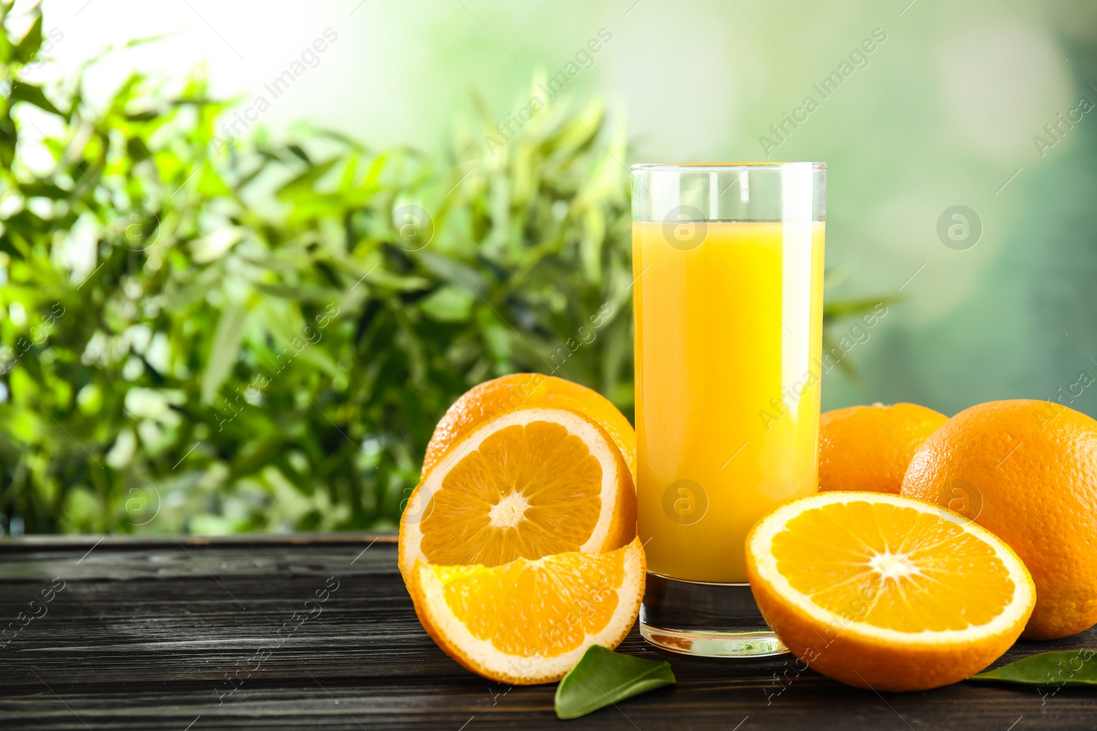 Photo of Glass with orange juice and fresh fruit on wooden table, space for text