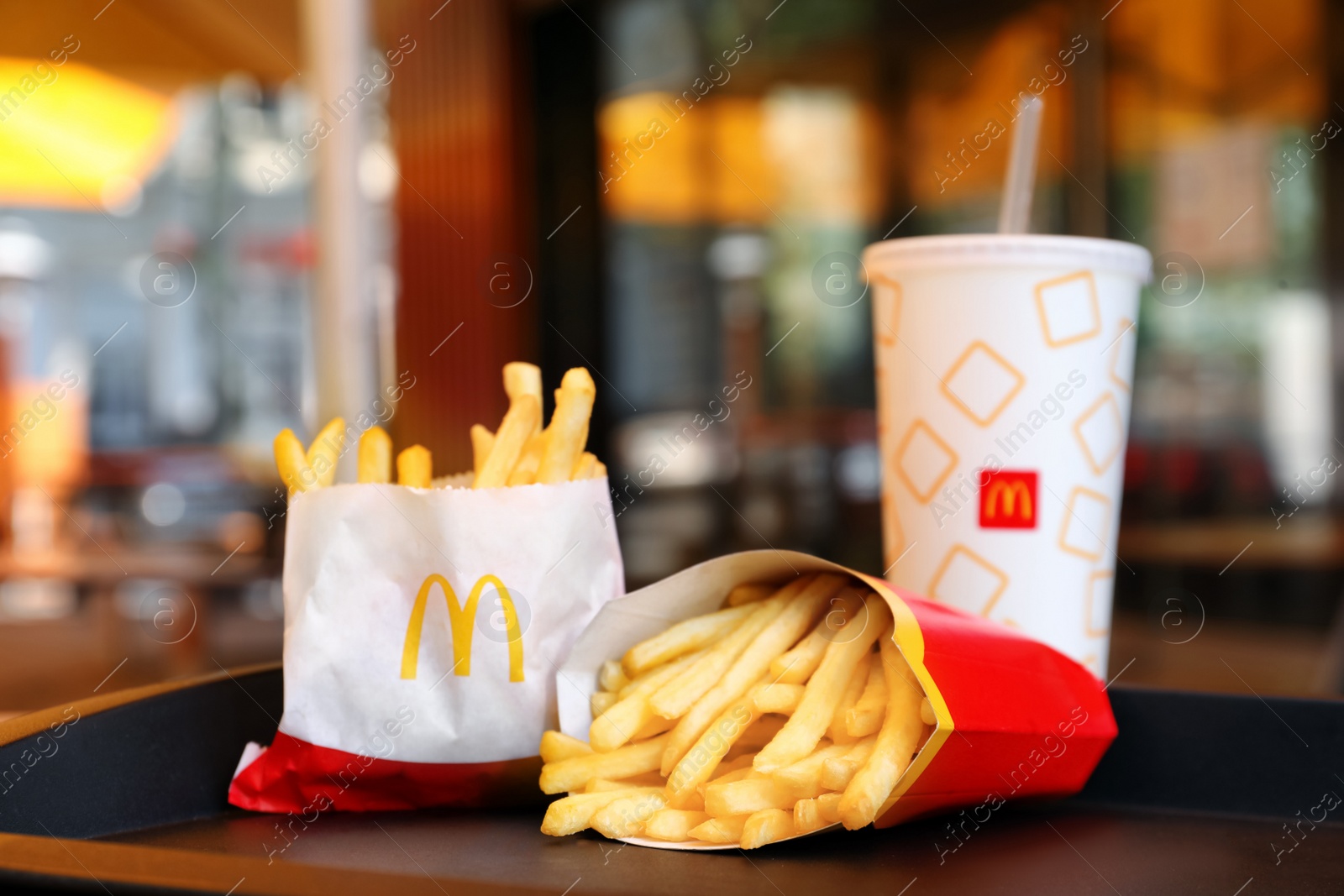 Photo of MYKOLAIV, UKRAINE - AUGUST 11, 2021: Big and small portions of McDonald's French fries near drink on tray in cafe