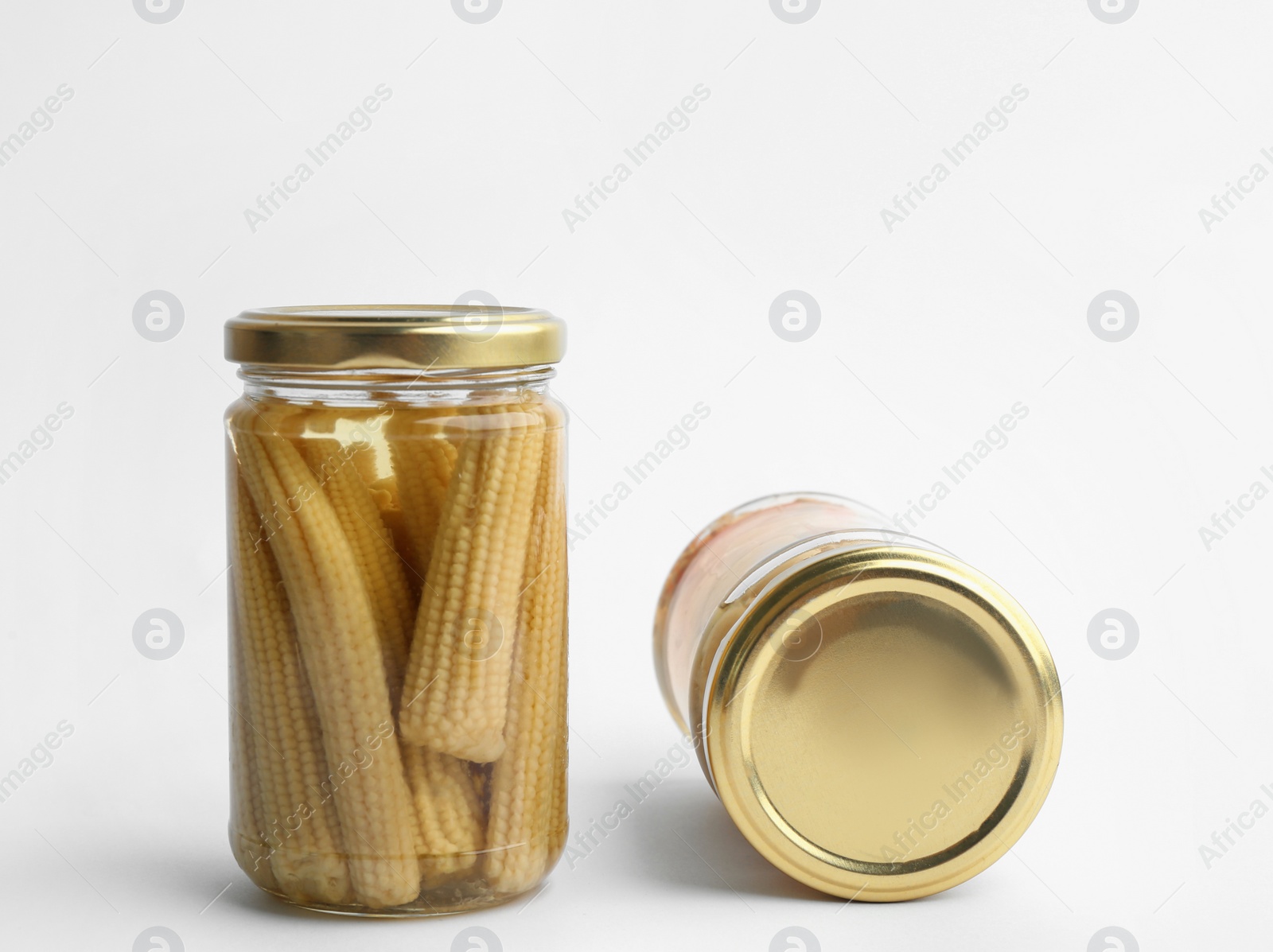Photo of Glass jars with pickled baby corn on white background