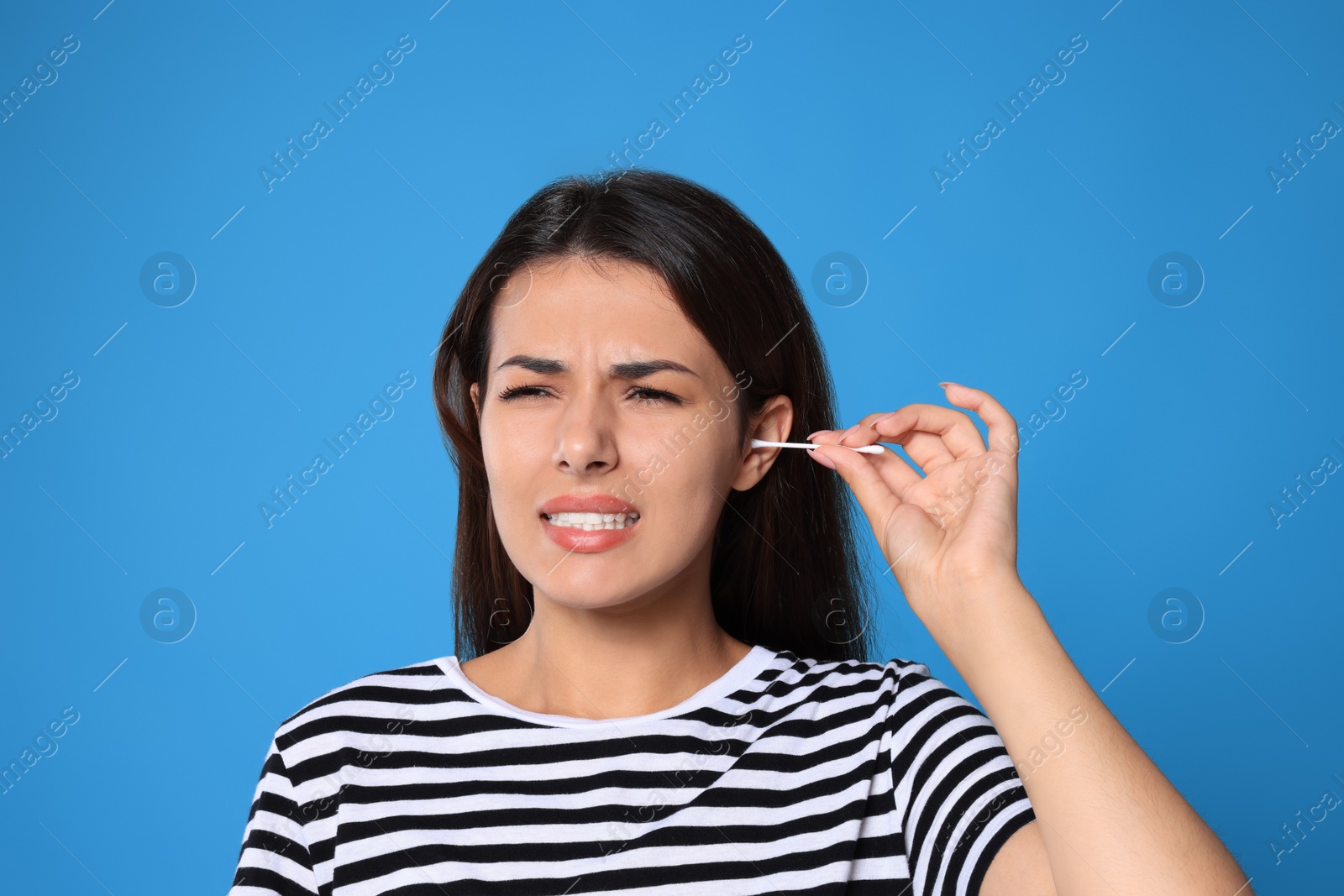 Photo of Young woman cleaning ear with cotton swab on light blue background