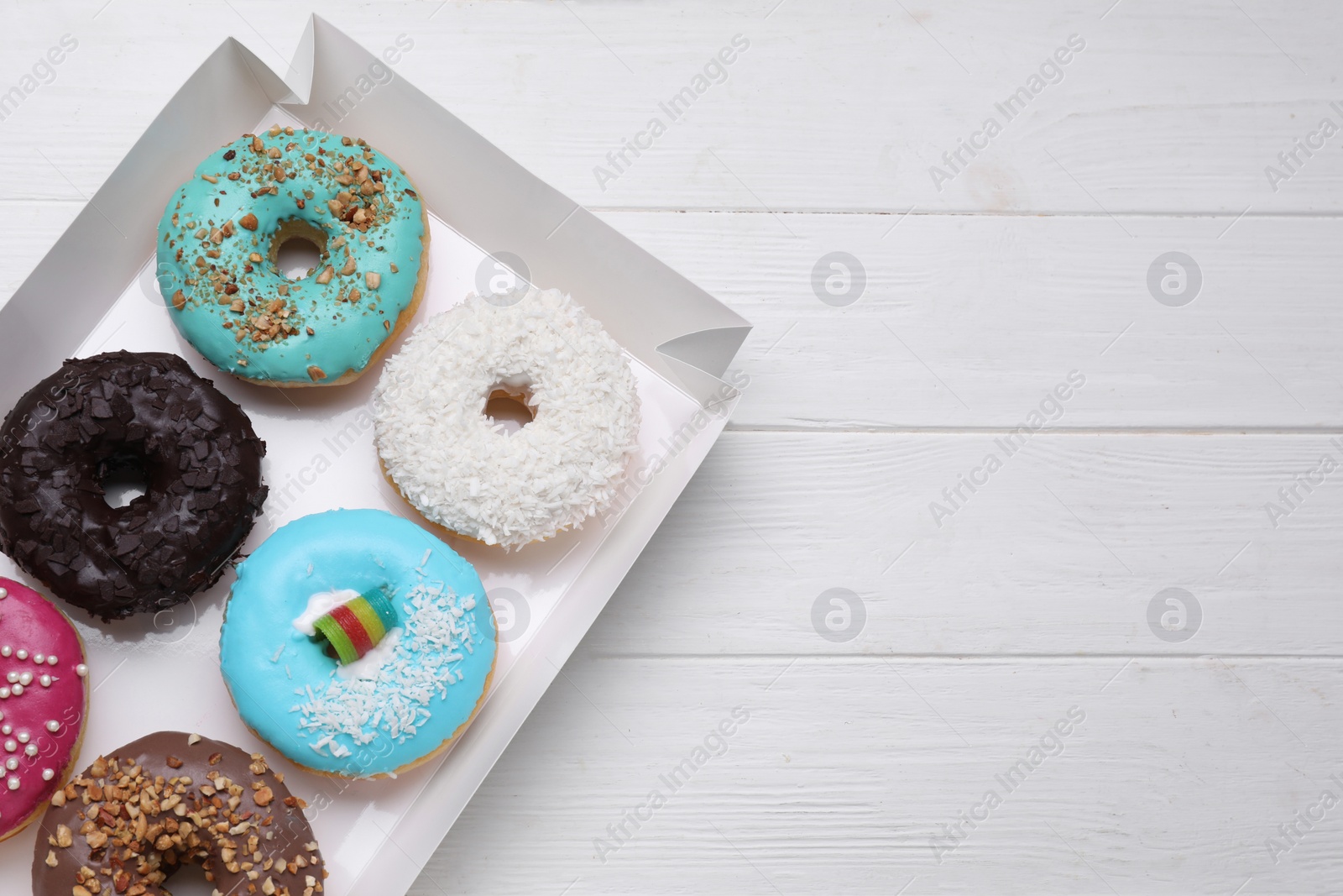Photo of Box with tasty glazed donuts on white wooden table, top view. Space for text