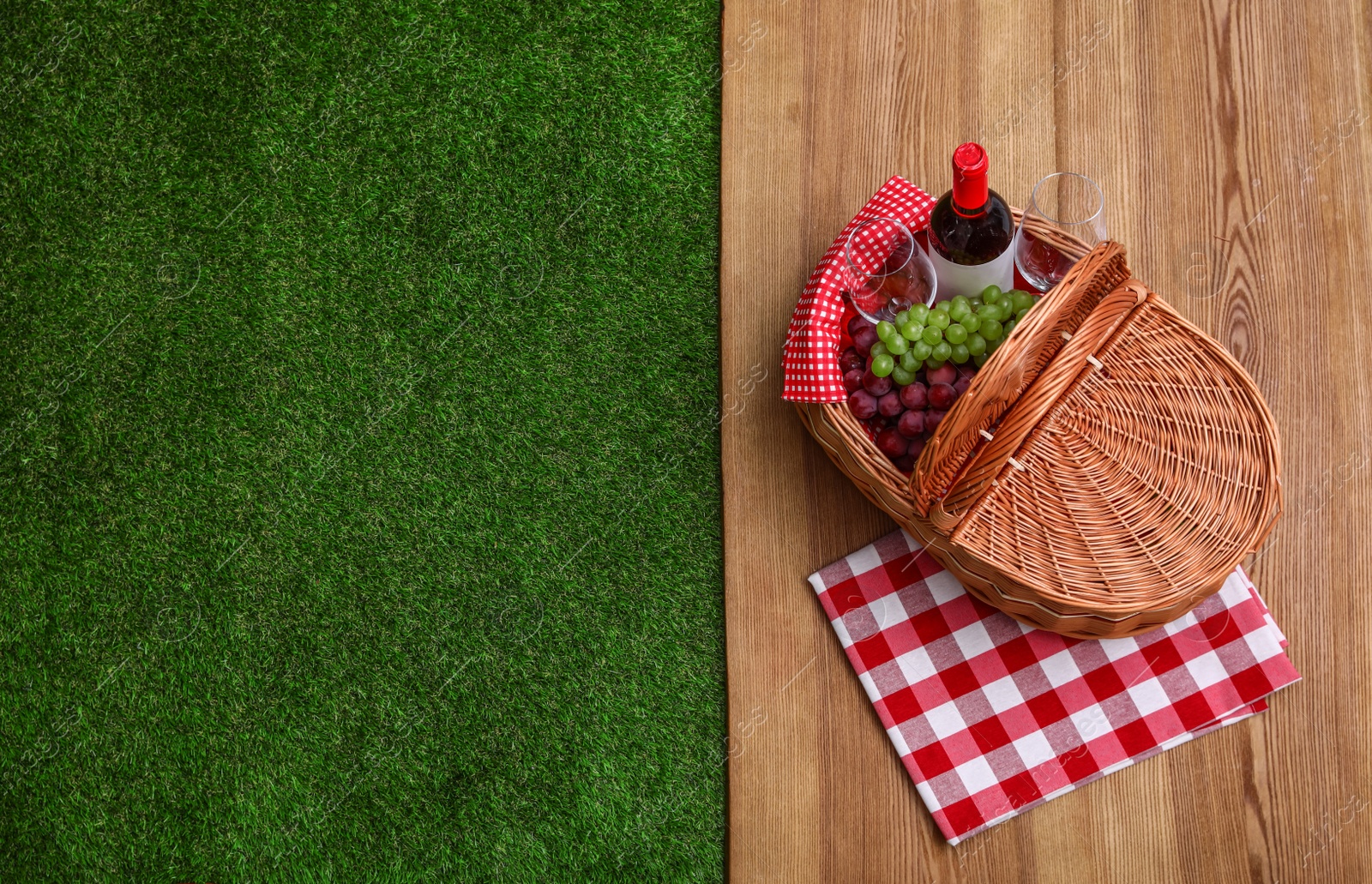 Photo of Picnic basket with wine and grapes on wooden surface outdoor, top view. Space for text
