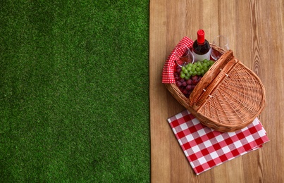 Photo of Picnic basket with wine and grapes on wooden surface outdoor, top view. Space for text